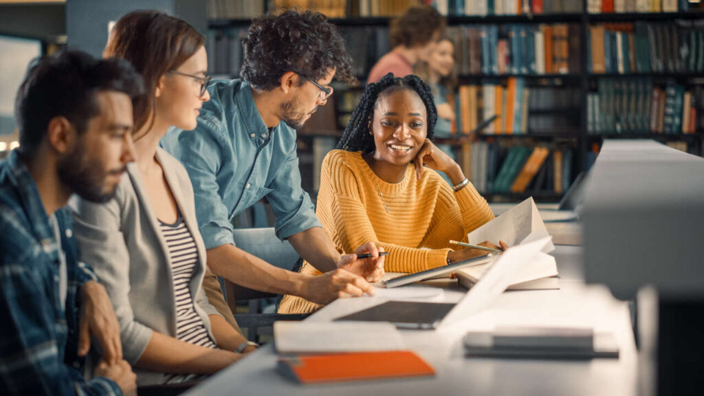 Quatro jovens sorridentes utilizando livros durante preparação para cursos de graduação mais procurados no Brasil.